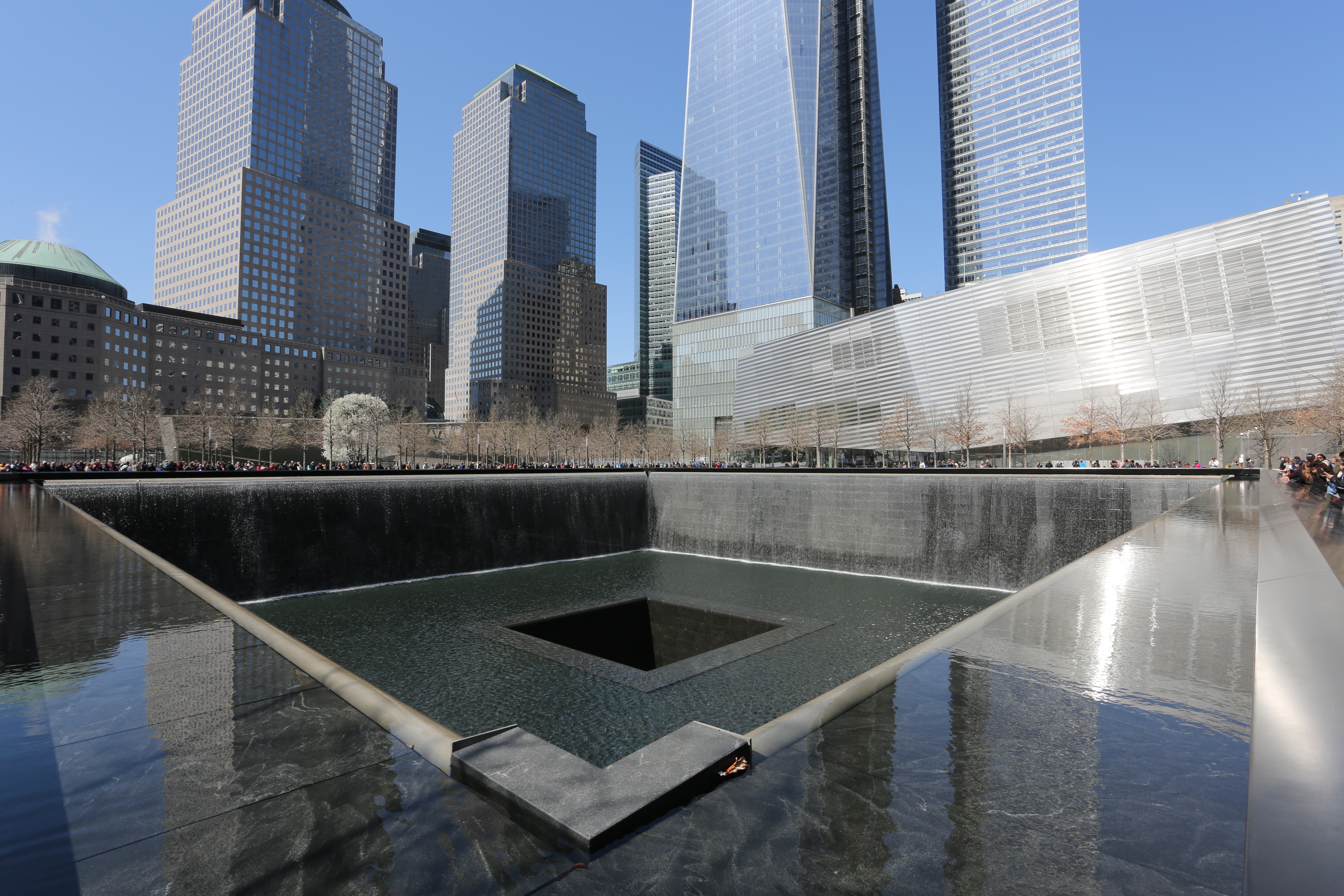 One of the Memorial’s waterfall pools is seen on a sunny, cloudless day in winter. The Museum pavilion, One World Trade Center, and other World Financial Center buildings are in the background.