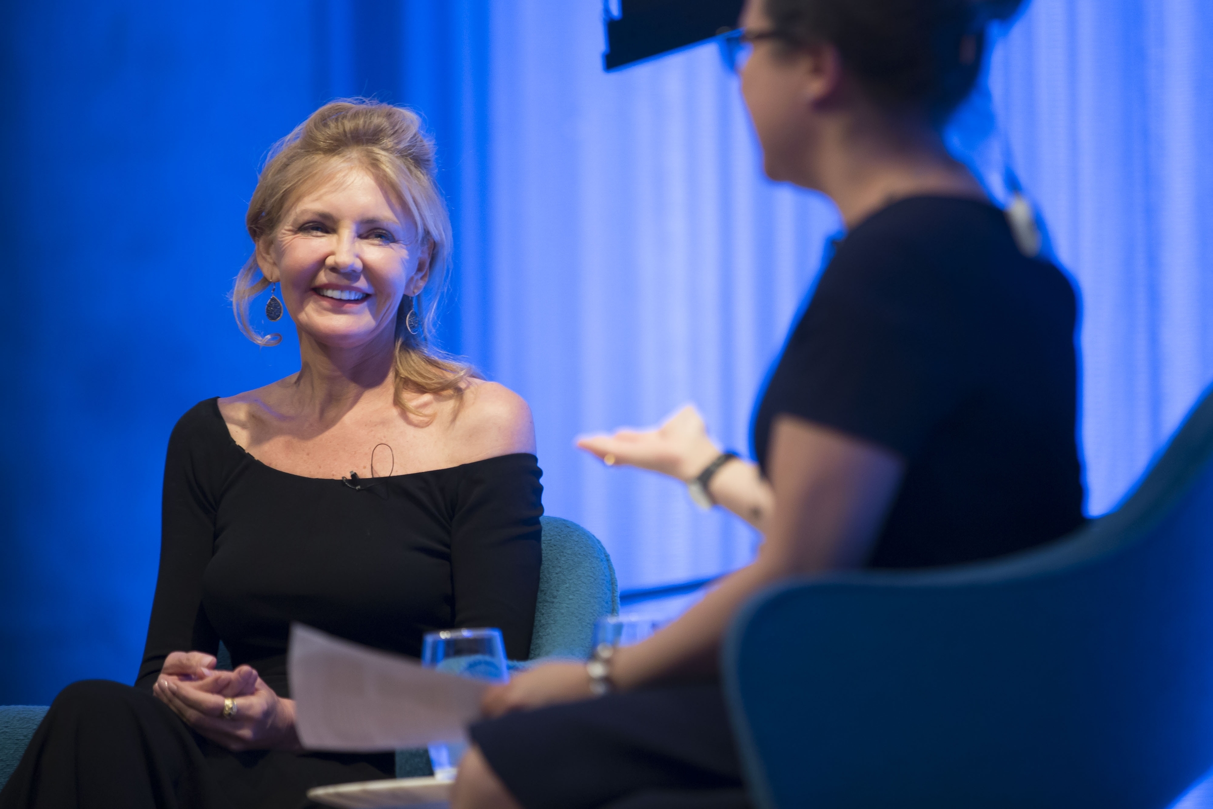 FEMA photographer Andrea Booher smiles onstage as she speaks with a woman out of focus in the foreground. 