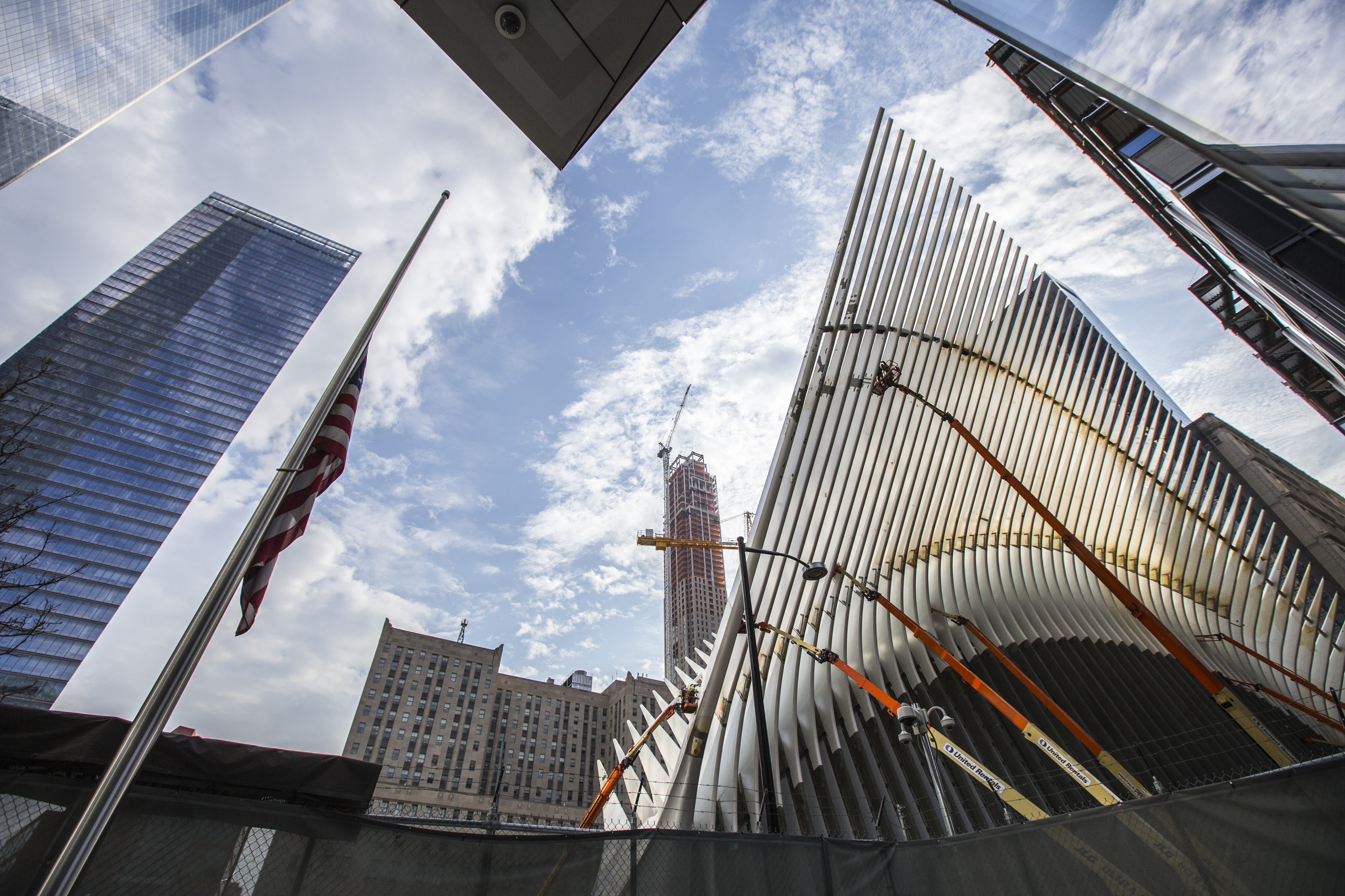 Workers on several cranes take part in the construction of the skeletal facade of the Oculus transportation hub. The buildings of lower Manhattan tower over the structure in the background.