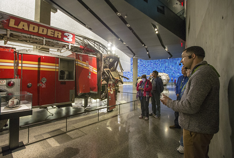 Several visitors listen to a tour guide as they stand beside the heavily damaged Ladder 3 fire truck.