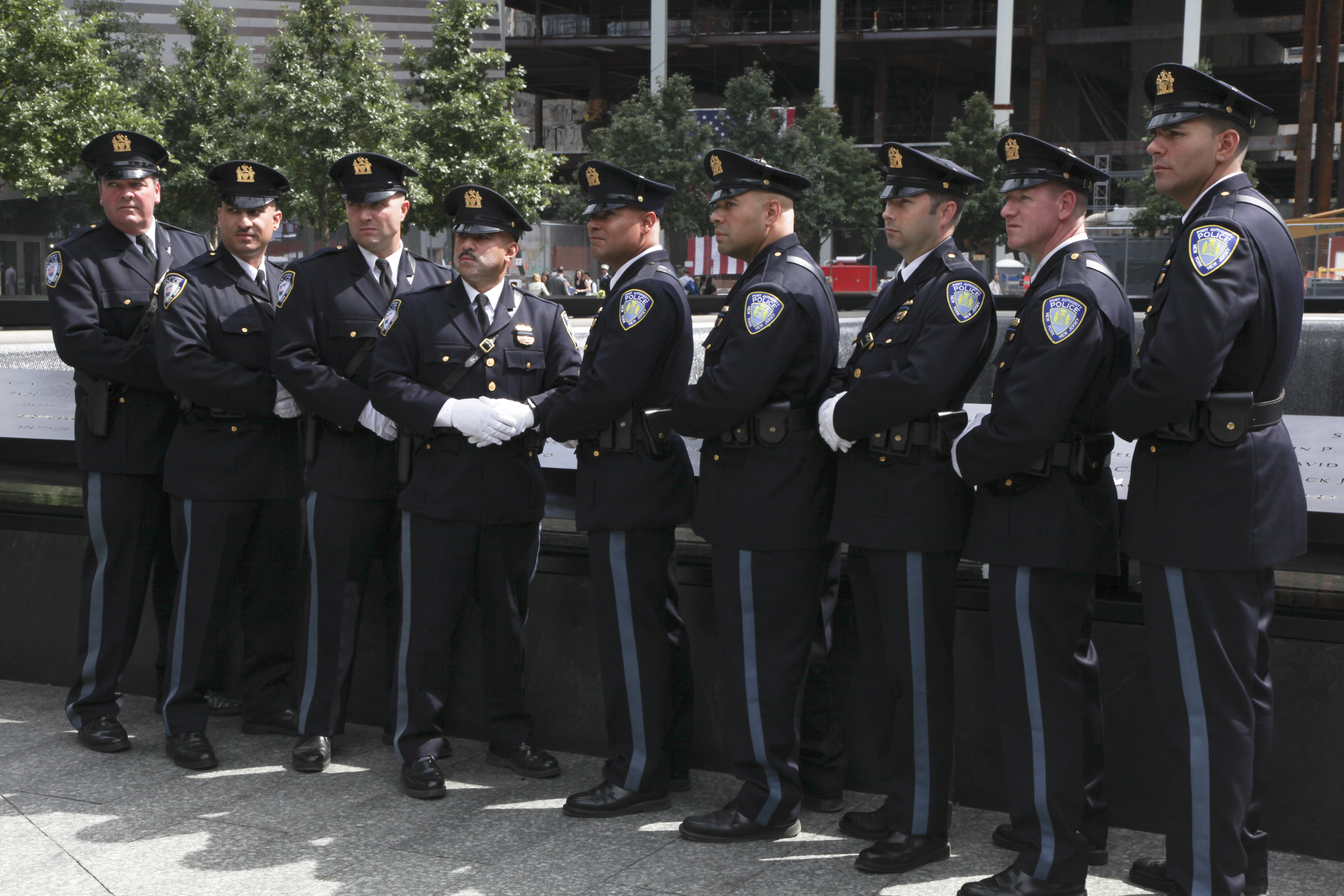 About a dozen NYPD officers in formal uniforms stand beside a reflecting pool at the 9/11 Memorial on the 10th anniversary of the 9/11 attacks.