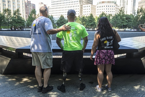 Three members of the Long Beach Waterfront Warriors—two men and one woman—look out at a reflecting pool while visiting Memorial plaza.