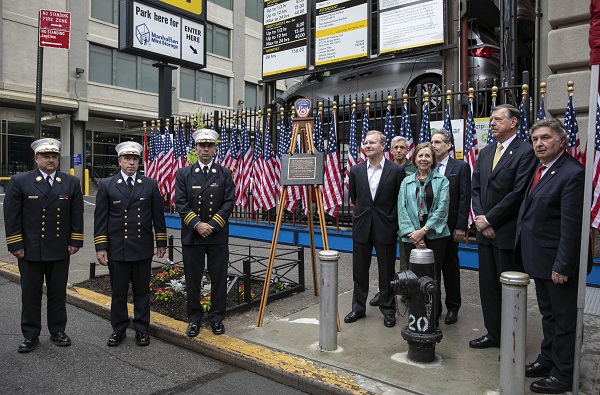 Representatives from the 8/11 Memorial & Museum and John Bowne High School attend a dedication ceremony of a Survivor Tree seedling in Flushing Queens. The attendees stand beside a tree and plaque.