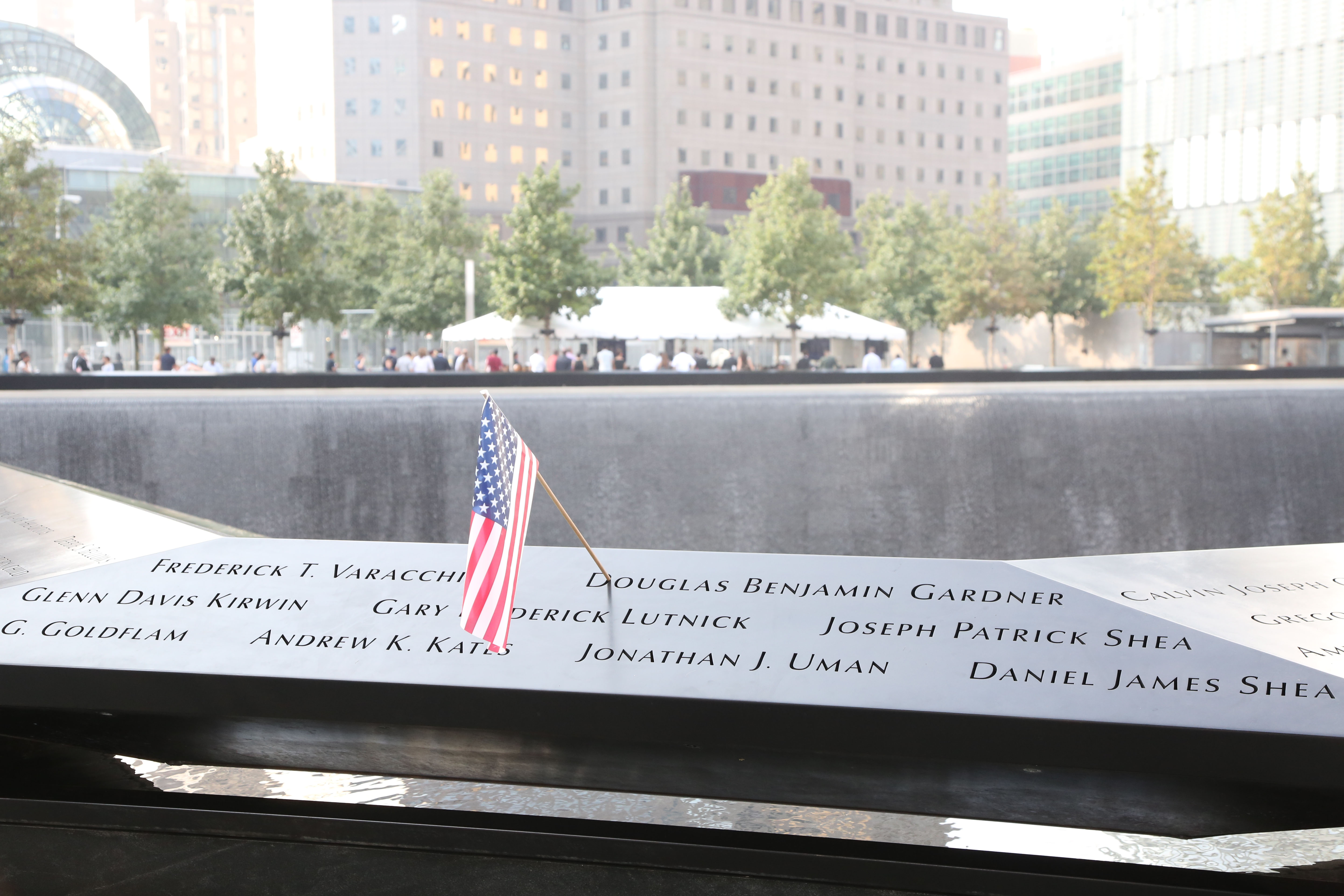 A small American flag has been placed at a name on a bronze parapet at the Memorial. The north reflecting pool is seen in the background.