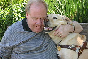 Michael Hingson embraces his guide dog Roselle in the shade of trees.
