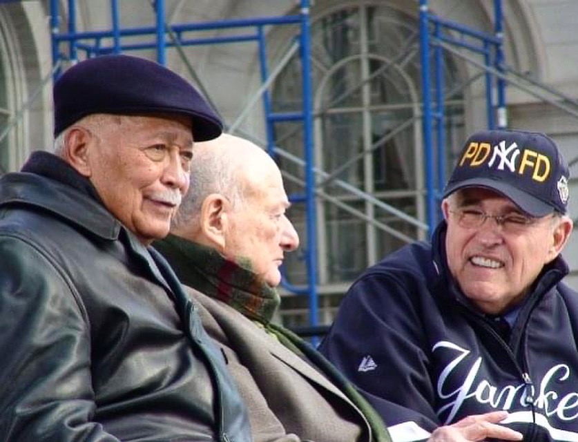 In this group photograph taken at City Hall in 2009, three former mayors are shown together from the waist up.   Mayor Dinkins, wearing a black cap and jacket, is looking ahead while Mayor Koch engages with Mayor Rudy Giuliani .