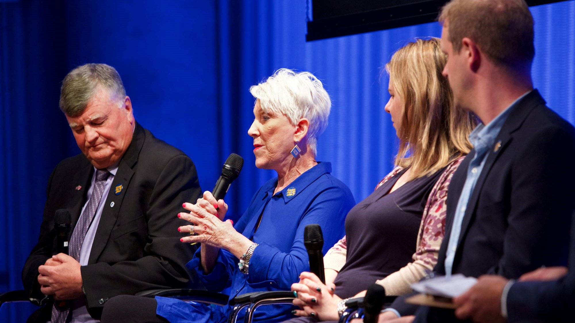 People behind the award-winning new musical “Come From Away” take part in the public program, Come From Away. They include a woman who is holding a microphone and speaking while looking towards the audience. Two men and a woman sit next to her as she speaks.