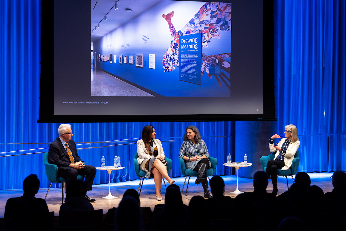 Four panelists sit on stage with a screen behind them featuring a photo of the opening of Drawing Meaning, an exhibition in the South Tower 