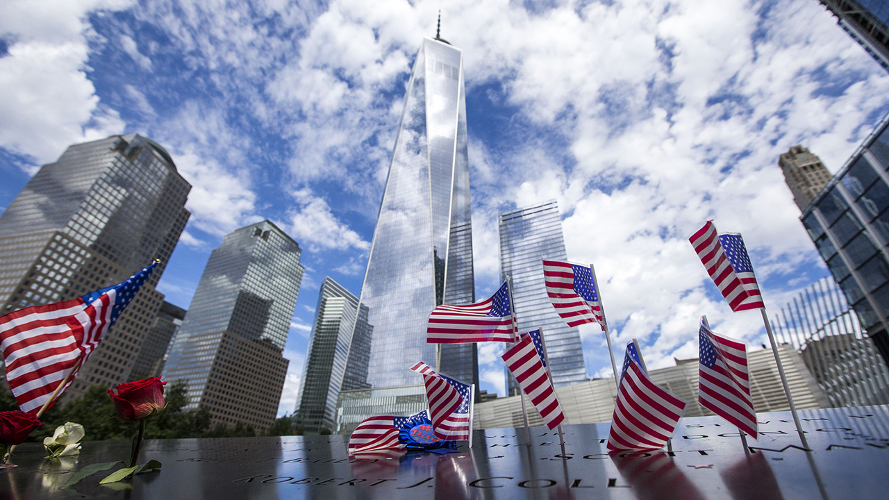 American flags are placed in the bronze parapets as One World Trade soars skyward amid white clouds and blue skies.