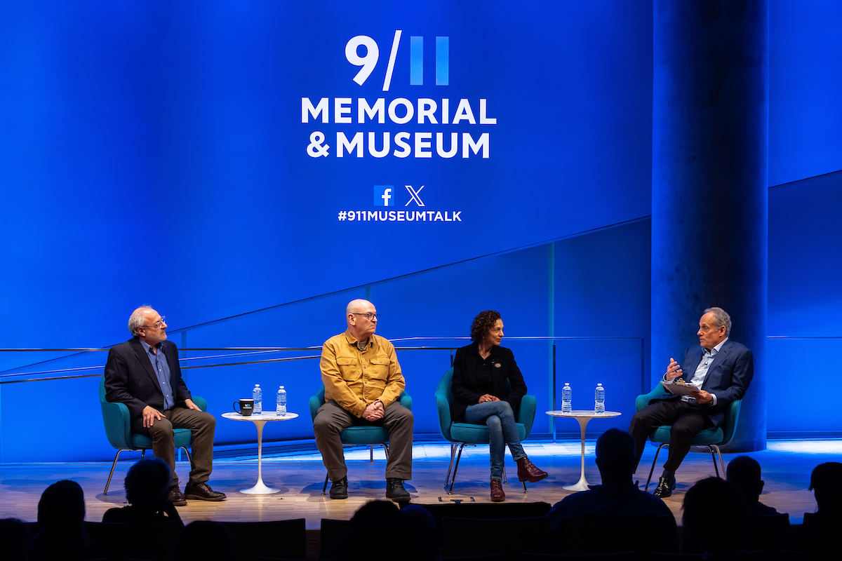 Four panelists seated on a stage with a giant screen behind them showing the opening 9/11 Memorial and Museum's logo and social icons