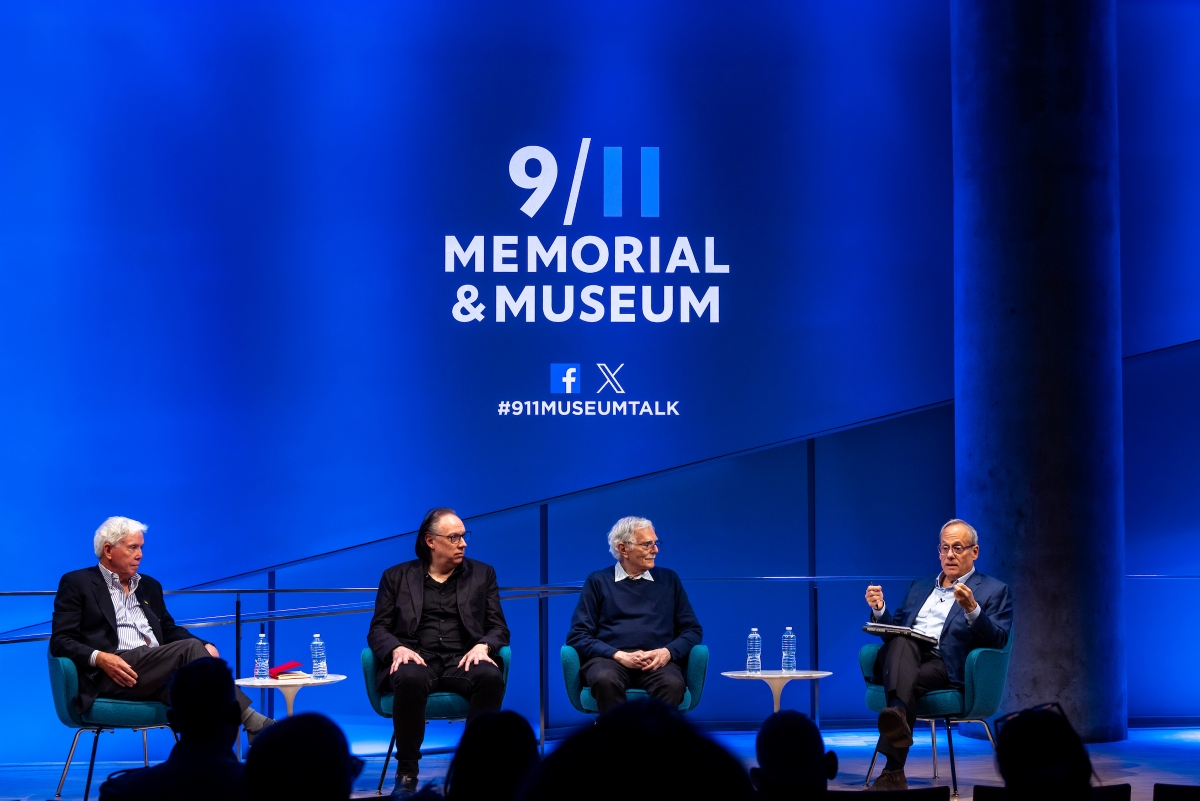 A panel sits on stage talking in front of a blue background