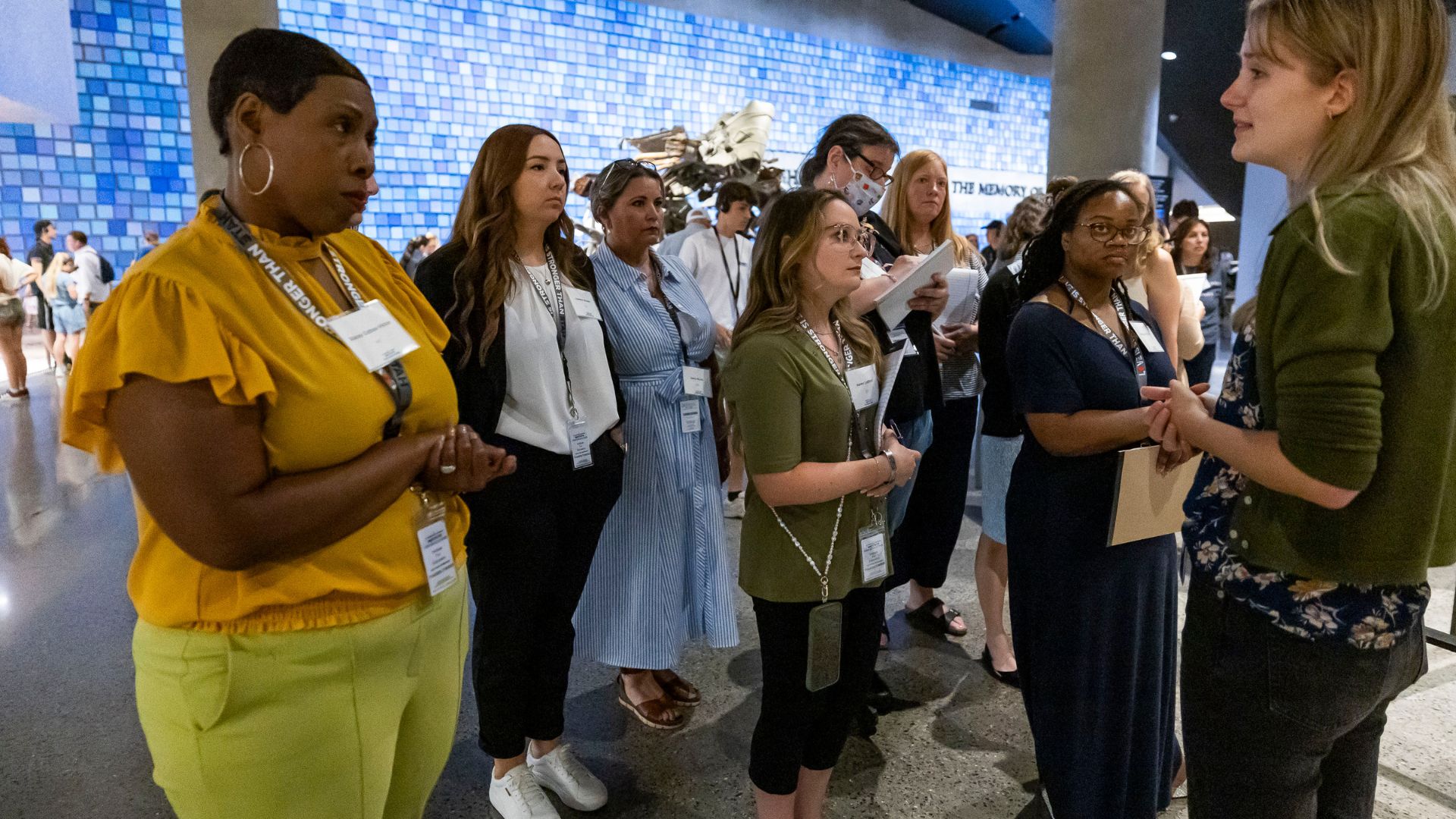 A group stands in front of a blue tiled wall, listening to a guide
