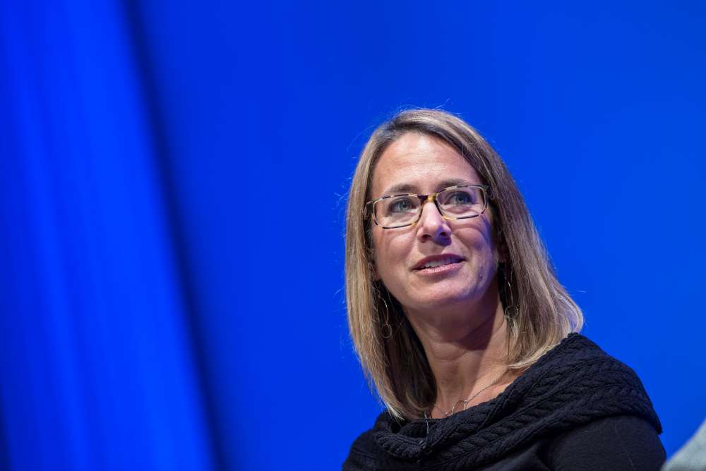 KBAS partner Julie Beckman speaks onstage as she takes part in the public program, The Architecture of Remembrance. The wall behind her is illuminated blue.