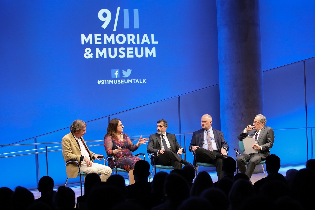 This wide-angle photo of the Museum Auditorium stage shows five people seated as they take part in a public program. Al-Qaeda expert Mary E. Galligan, sitting second from the left, speaks as the other attendants listen on. Al-Qaeda expert Peter Bergen sits to her right. Three other men are seated to her left—al-Qaeda expert Bruce Hoffman, Museum advisor Mark Stout, and Clifford Chanin, the executive vice president and deputy director for museum programs. About a dozen audience members watch on in the foregr