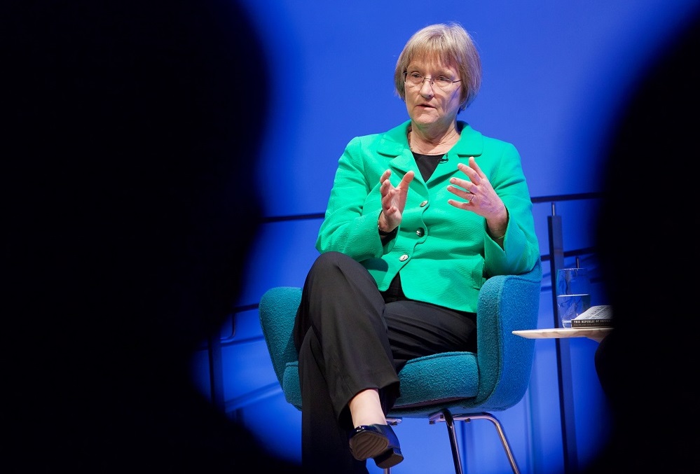 A woman in a green suit jacket appears through the silhouetted heads of audience members in a 9/11 Memorial Museum public program.