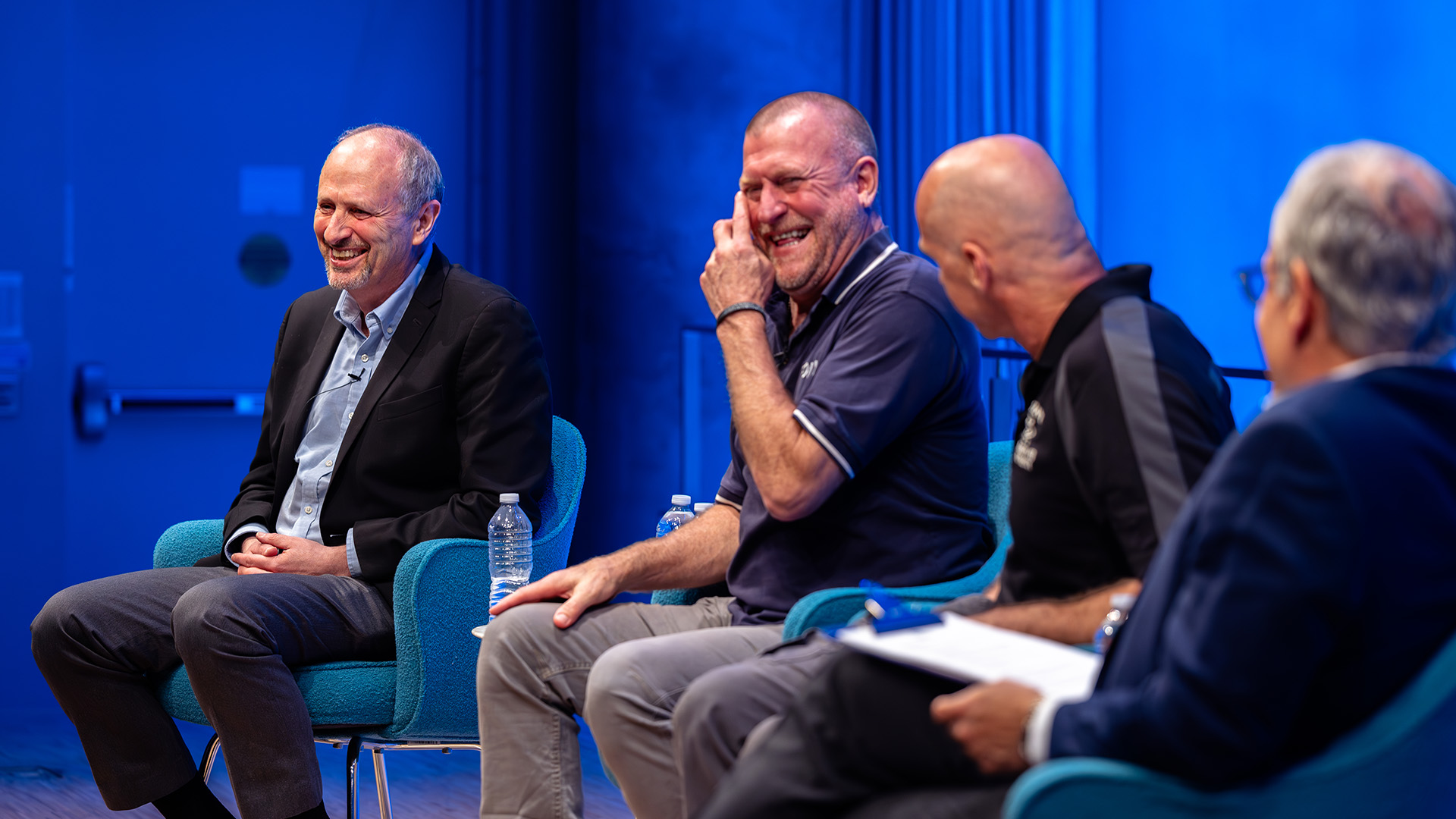 four speakers sitting on stage, laughing enthusiastically.