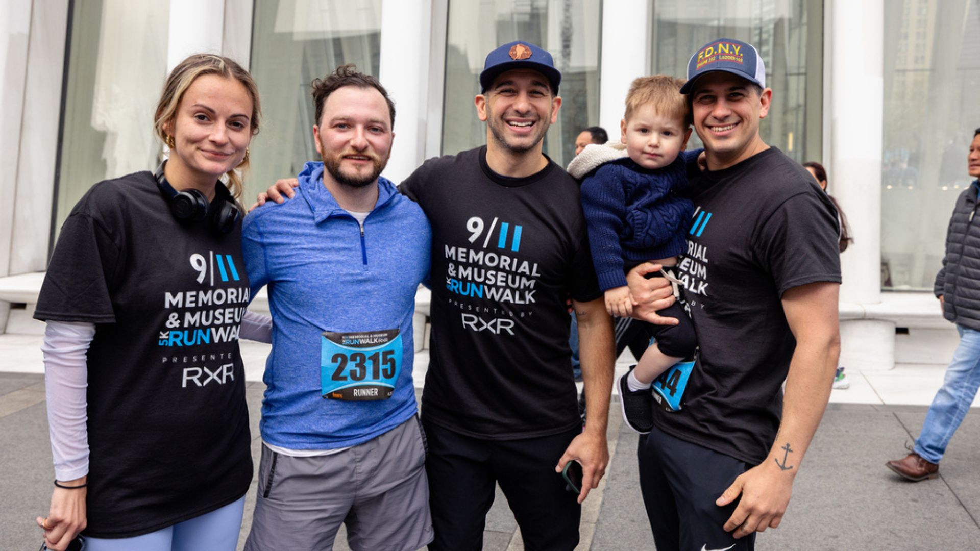 Four adult Visionaries wearing 9/11 5k t-shirts link arms and smile. One Visionary is holding a toddler.