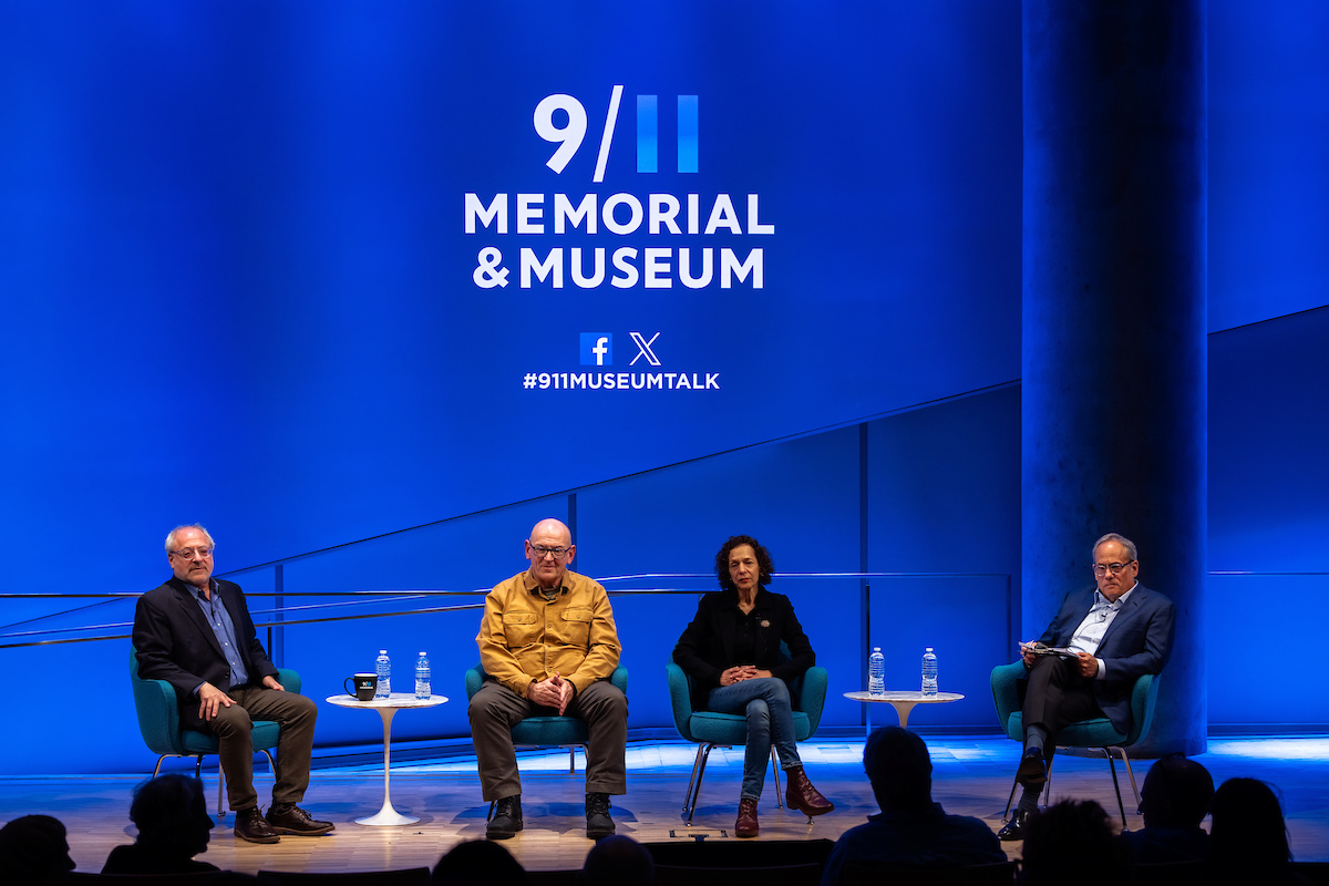 Four people sit on a stage, behind them is a blue banner or screen with 9/11 Memorial & Museum's logo and social icons visible