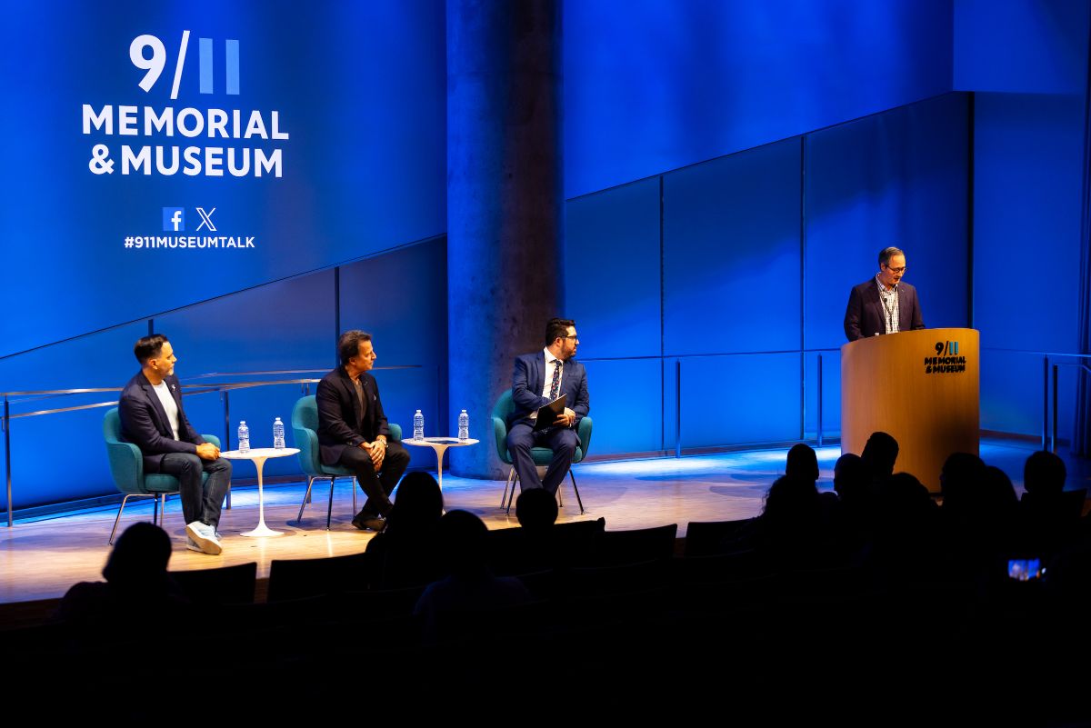 Four people sit on a stage, behind them is a blue banner or screen with 9/11 Memorial & Museum's logo and social icons visible