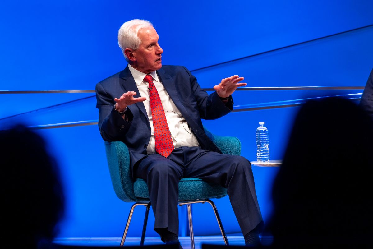 a man in a red tie and suit gestures and speaks