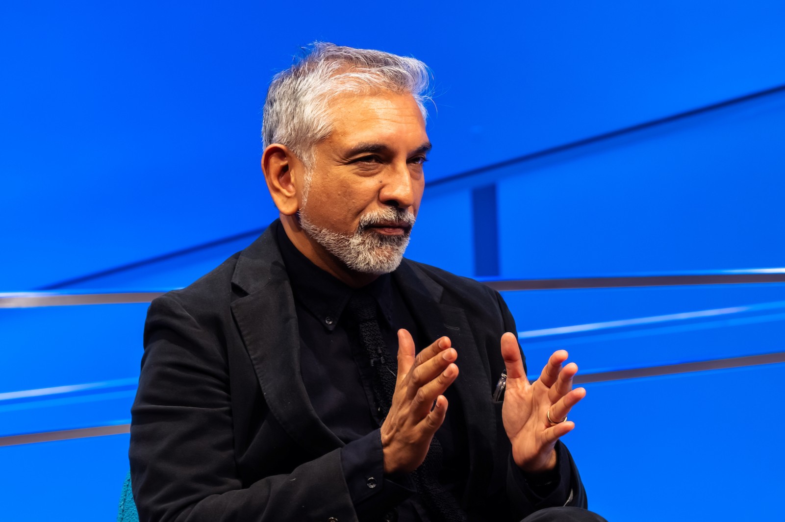 a man in a dark suit gestures with two hands
