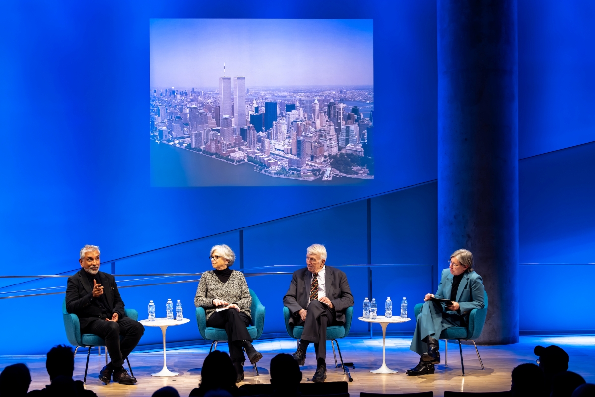 Four people sit on stage with an image of the WTC site on view behind them