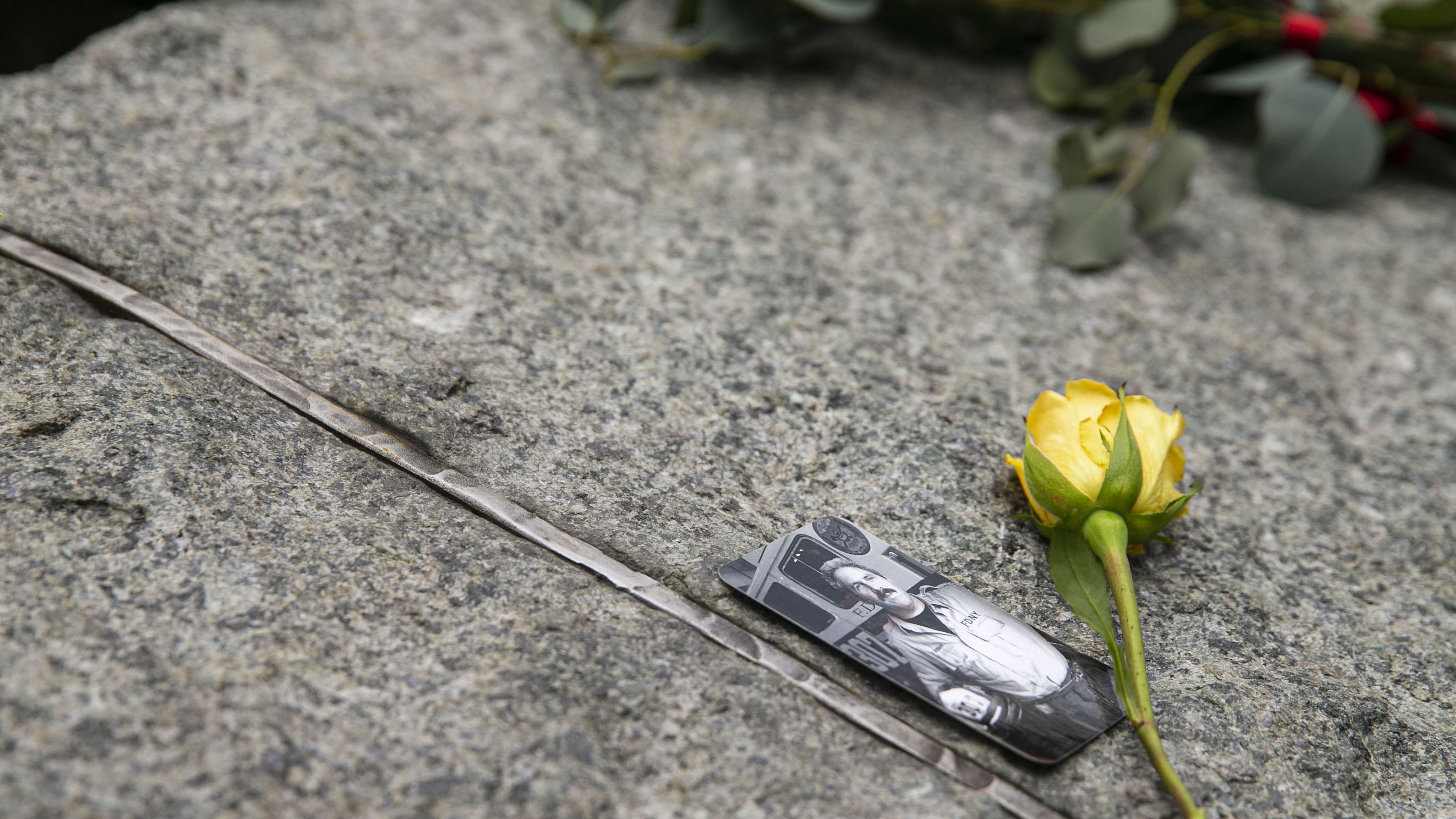 A photo of a man in front of an FDNY fire truck has been placed on a stone monolith at the Memorial Glade, which honors sick and fallen rescue and recovery workers. A yellow rose has been placed to the right of the photograph.