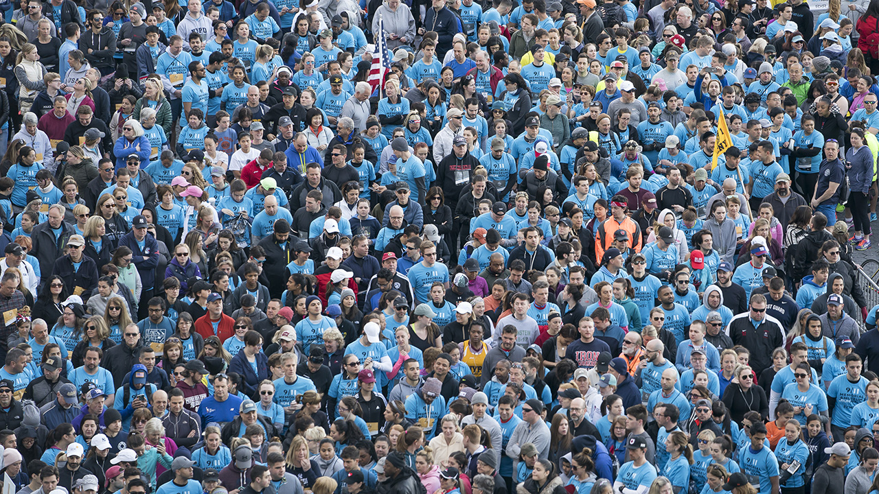 Hundreds of participants, many of them wearing light blue T-shirts, gather together at the annual 5K Run/Walk in this aerial photograph.