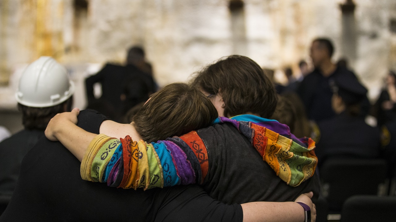 Two women embrace while standing in a crowd beside the slurry wall in Foundation Hall.