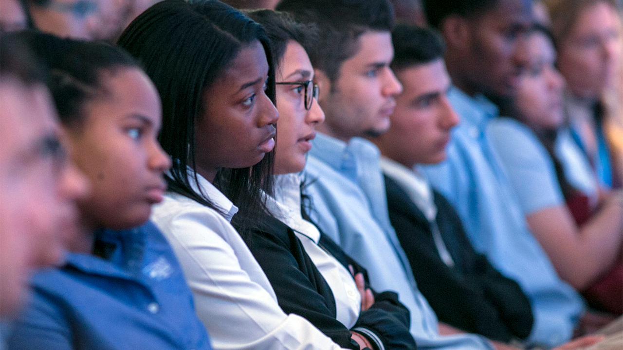 Students sit in a row as they look forward and listen to a speaker who is out of view in the Museum auditorium.