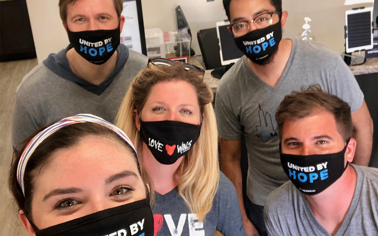 Five people, two women and three men from the USO and the 9/11 Memorial Museum,  smile for the camera as they wear 9/11 Memorial Museum masks as part of the effort to distribute masks to first responders. 