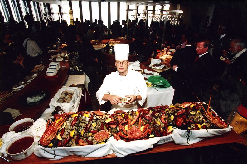 High angle view of a male chef standing in front of a table spread filled with seafood. 