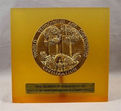 Orange-hued square plague with bronze seal in the upper center depicting the Twin Towers with smoke billowing out. Text written around the seal reads: "World terrorists are destroying civilization." 