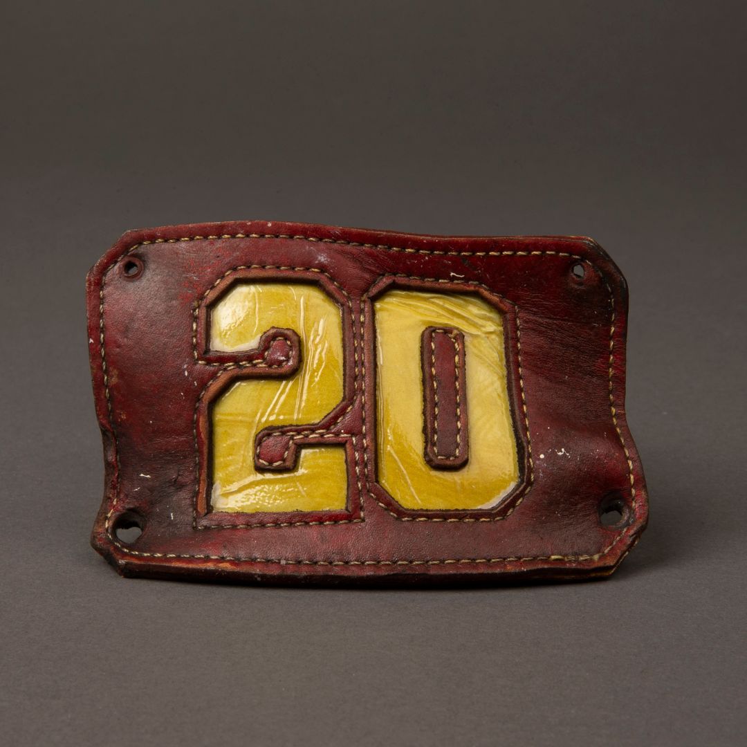 Visibly misshapen front piece from FDNY firefighter helmet, with the number 20 in yellow gold against a dark red background