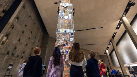Back view of four children looking up at the Last Column, which is covered in memorial graffiti and other items of remembrance like photos and notes