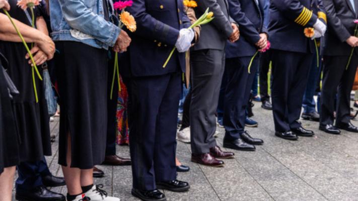 Waist-down view of crowd gathered on the Memorial Glade, many holding flowers