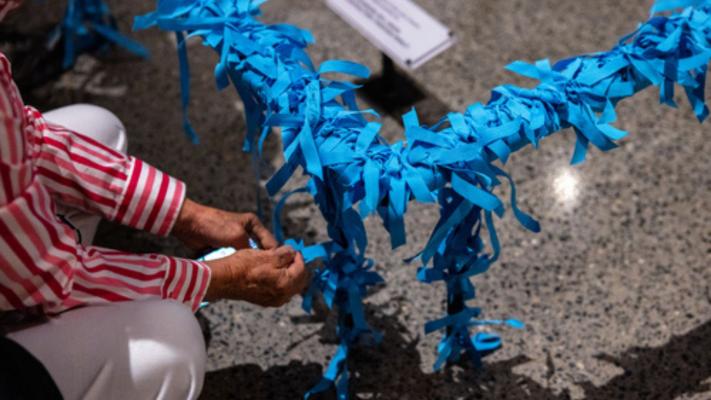 Hands tying blue ribbons at the base of the Last Column in the Museum