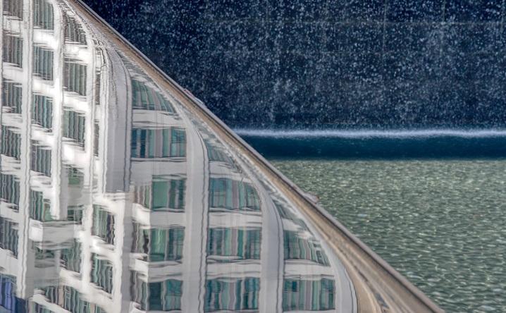 In a close-up view, a building reflects off the 9/11 Memorial as water cascades down into a reflecting pool.