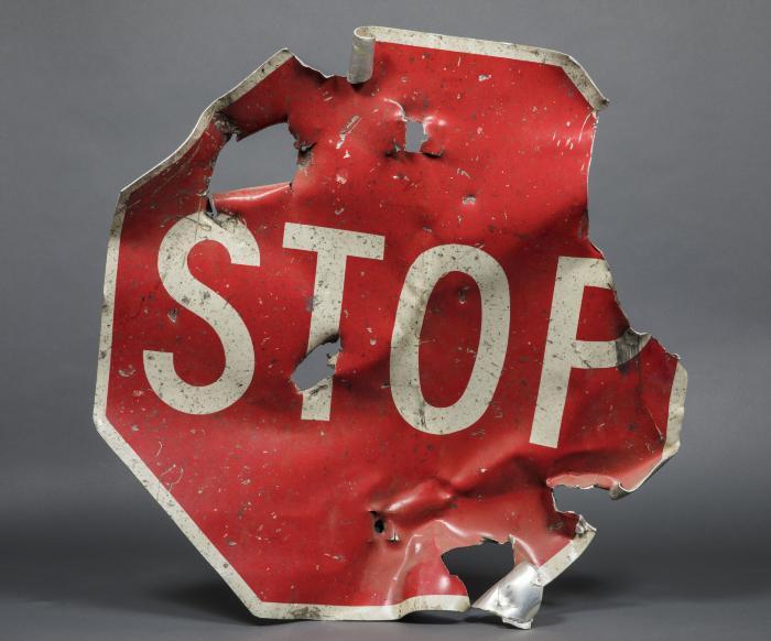 A red stop sign that was partially destroyed in the 1993 bombing of the World Trade Center is displayed on a gray surface at the Museum.