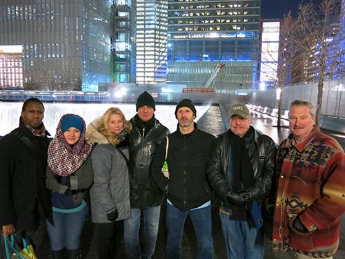 The cast and crew of “Bikeman” stand beside a reflecting pool at Memorial plaza. They include Irungu Mutu, Elizabeth Ramos, Angela Pierce, Robert Cuccioli, Richard Topol, director Michael Bush, and author Thomas F. Flynn.