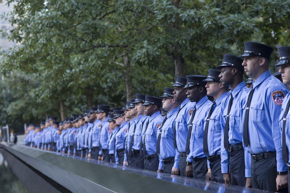 A probationary class of FDNY EMTs stands in front of a reflecting pool at the 9/11 Memorial.