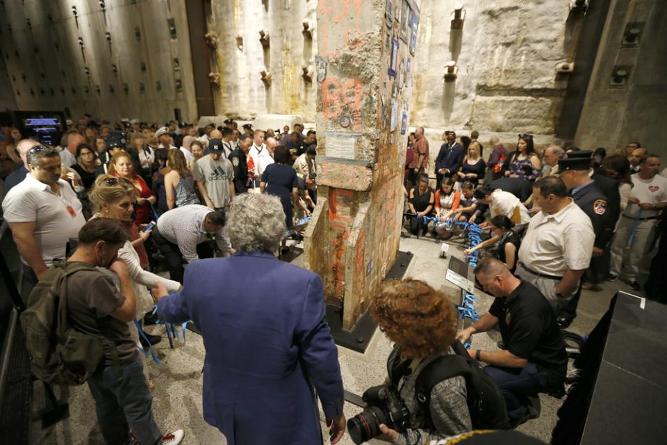 Dozens of participants take part in a ceremony at the Last Column. Some of them are playing blue ribbons on a railing surrounding the column.