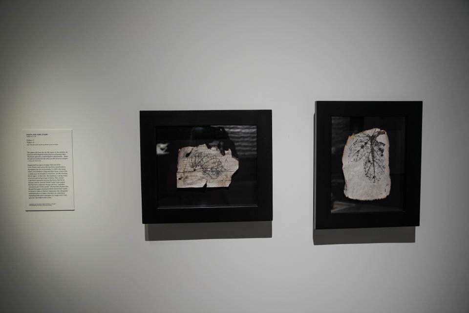 Two framed pieces of artwork from Doug and Mike Starn are displayed on a white wall. The artwork features singed and torn paper that blew out of the towers. 