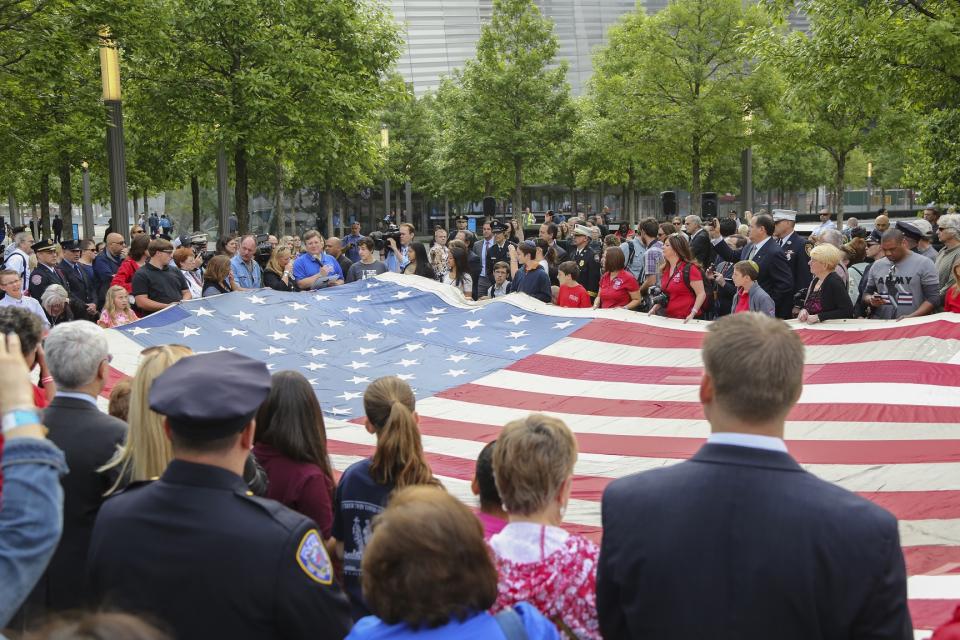Dozens of people stand in Memorial plaza as they hold up a large American flag during the opening of the Museu in May 2014.