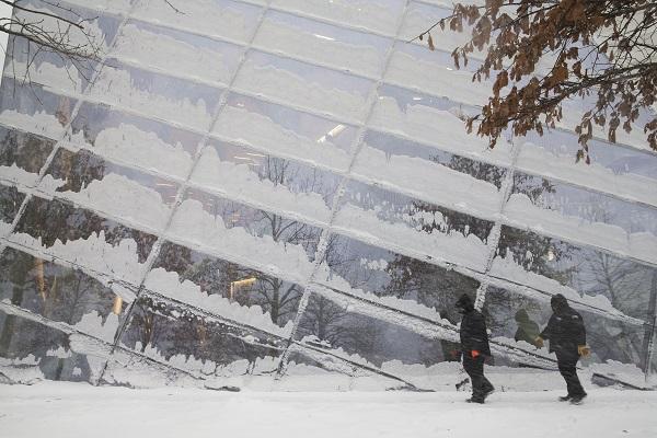 Snow covers the windows of the Museum pavilion as two warmly dressed workers walk by during a winter storm.