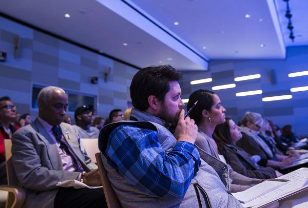 Educators look on from the audience as they take part in the Chancellor’s Day Professional Development workshop in the Museum auditorium. A man in the foreground has placed his fingers to his lips as he listens intently.