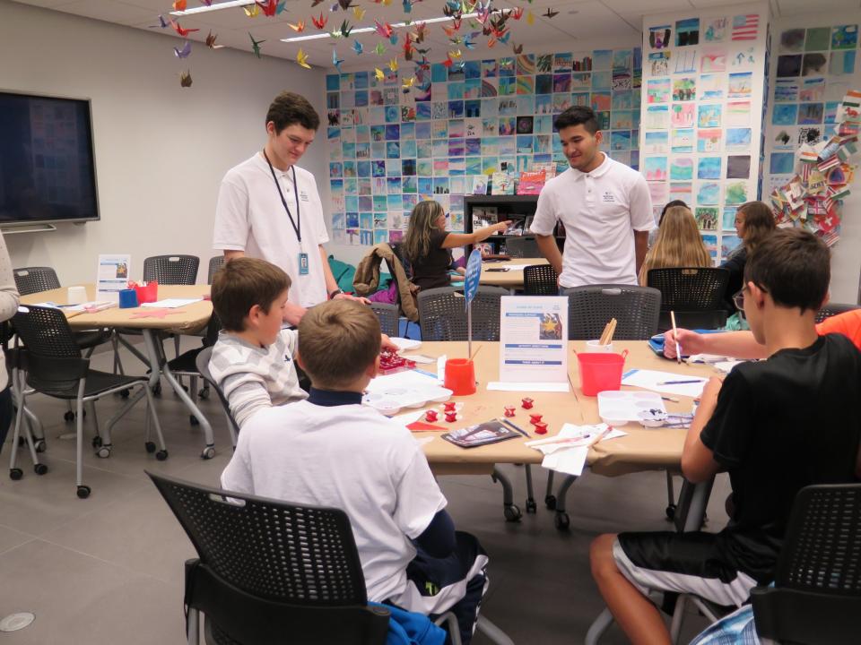 Two instructors stand over a table as several boys work on projects in the Education Center at the Museum.