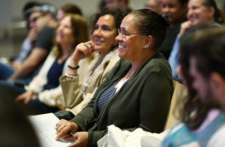 A woman among in a row of people in an auditorium, and smiles.