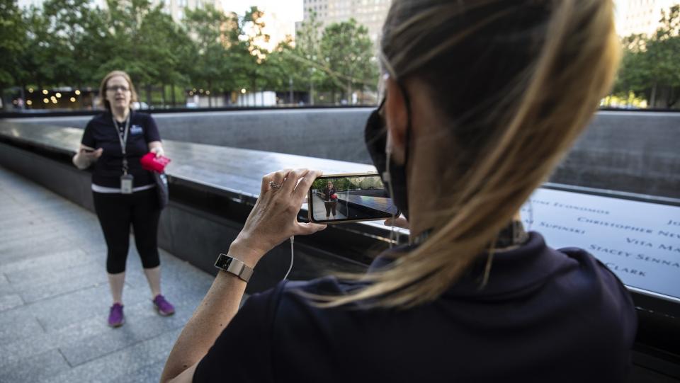 A woman uses a smartphone to film another woman addressing the camera at the 9/11 Memorial.